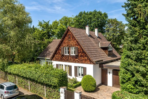 Die Fassade begeistert mit Sprossenfenstern, Holzläden und Schindelverkleidung