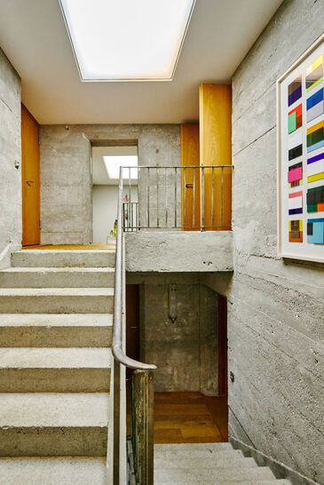 Stairwell of raw exposed concrete with a skylight, a large colour field painting on the wall.
