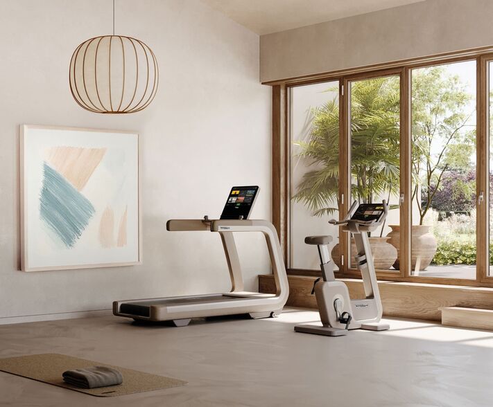 Heller Trainingsraum mit Laufband und Ergometer vor bodentiefen Fenstern, an der Wand ein abstraktes Bild.