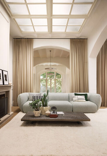 Light-coloured, rounded sofa in a high-ceilinged room with a stucco ceiling and floor-to-ceiling windows.