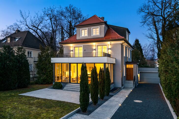 Modern villa with a round tower and large glazed areas glowing warmly from within at dusk.