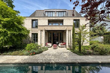 Symmetrical natural stone villa behind an elongated pool lined with red armchairs and trees.