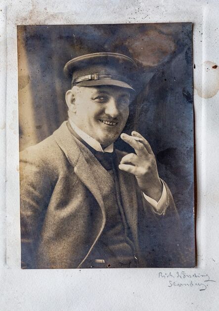 Historische Sepia-Aufnahme eines Mannes mit Schirmmütze und Schnurrbart, der eine Zigarre in der Hand hält.