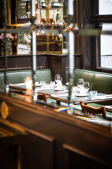 Bistro dining room with green leather banquettes, tables with white cloths, brass lamps and a mirrored wall.