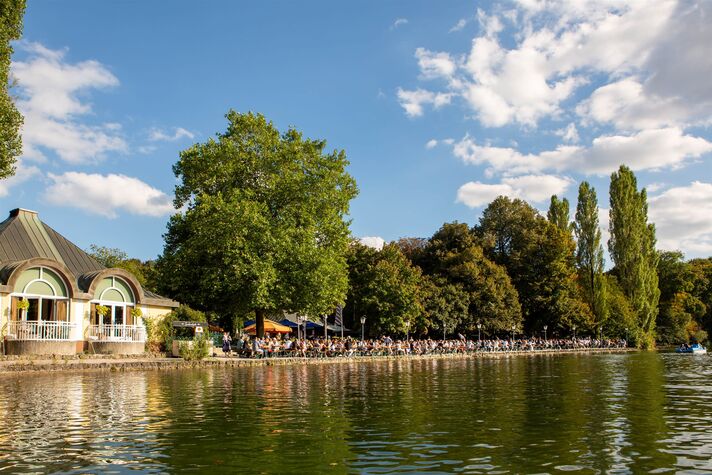 View across Kleinhesseloher See to the Seehaus with its busy beer garden under tall trees.