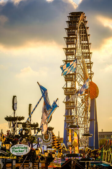Beleuchtetes Riesenrad und Fahrgeschäfte drehen sich in der Abenddämmerung über den Köpfen der Besucher.