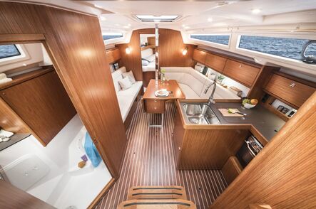 Salon einer Segelyacht mit heller Polsterbank, Holzausbau, Pantry und gedecktem Klapptisch.