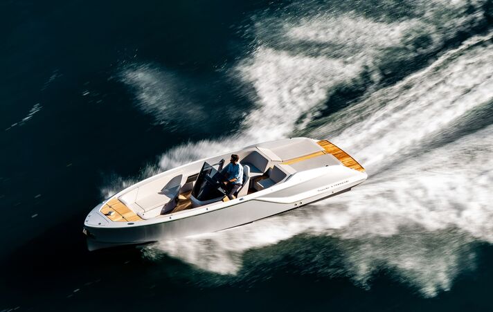 Schräg von oben aufgenommenes Elektro-Dayboat mit heller Holzbeplankung, das eine breite Schaumspur hinter sich herzieht.