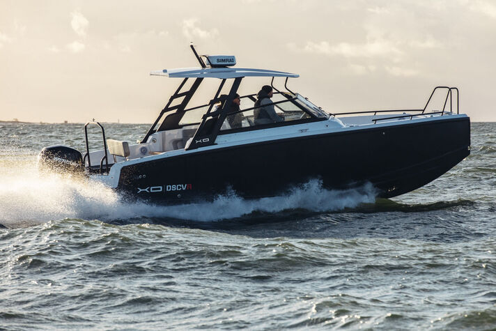 Dunkles Aluminium-Motorboot mit festem Hardtop pflügt bei bewölktem Himmel durch bewegtes Wasser.