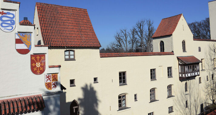 White rendered wings of Grünwald Castle with a red tiled roof, painted coats of arms on the façade and a wooden oriel.