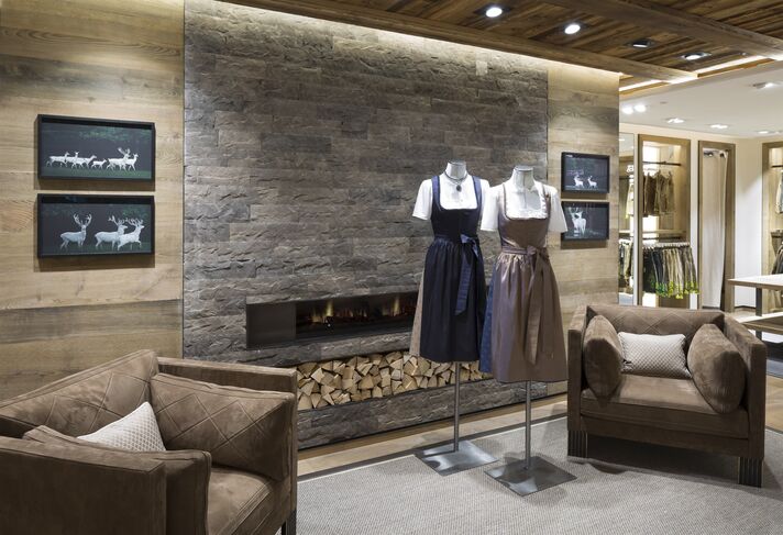 Shop floor with a stone wall, fireplace and leather armchairs, with busts displaying dirndls and traditional jackets in front.