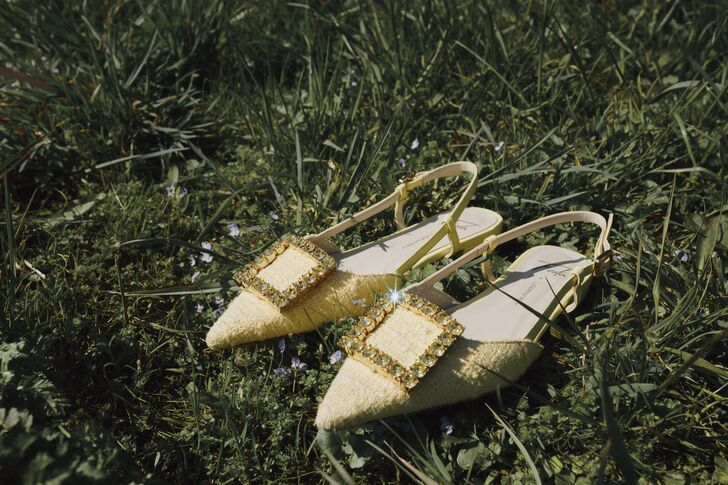 A pair of pale yellow studded slingbacks in the grass of a summer meadow.