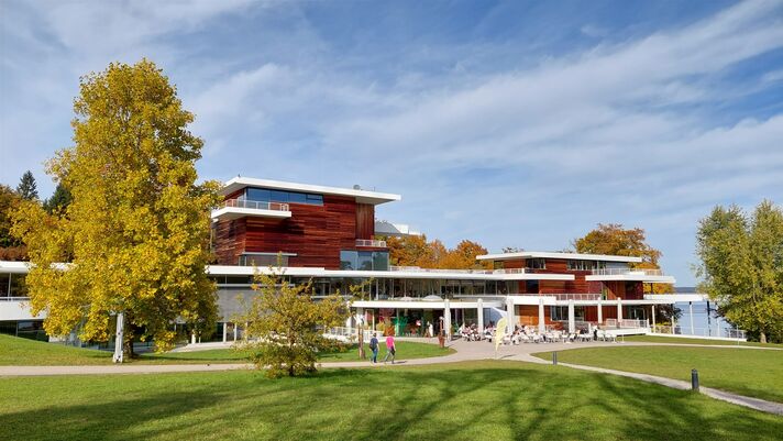 Langgestreckter Museumsbau mit Glasfront und auskragendem Dach im Park, davor Rasen und alte Bäume.