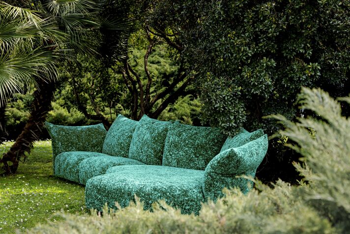 Großes modulares Sofa mit petrolfarbenem, gemustertem Outdoorbezug steht auf einer Wiese vor dichtem Grün.