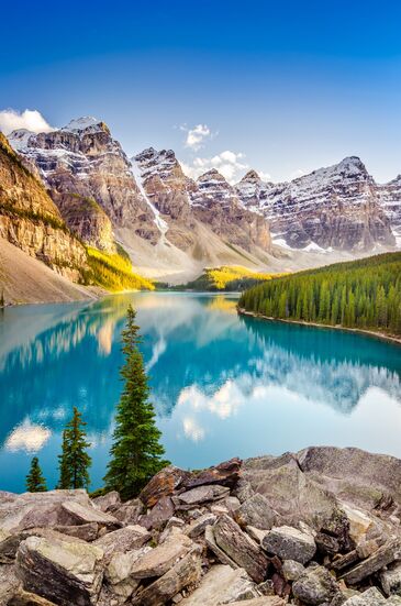 Turquoise mountain lake between rugged peaks, with large boulders on the shore in the foreground.
