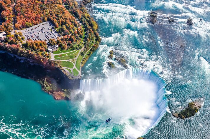 Aerial view of the horseshoe-shaped waterfall, with turquoise water plunging over its edge into a cloud of spray.