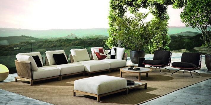 Cut-out long modular sofa with olive green upholstery, a wooden frame and loosely placed cushions.