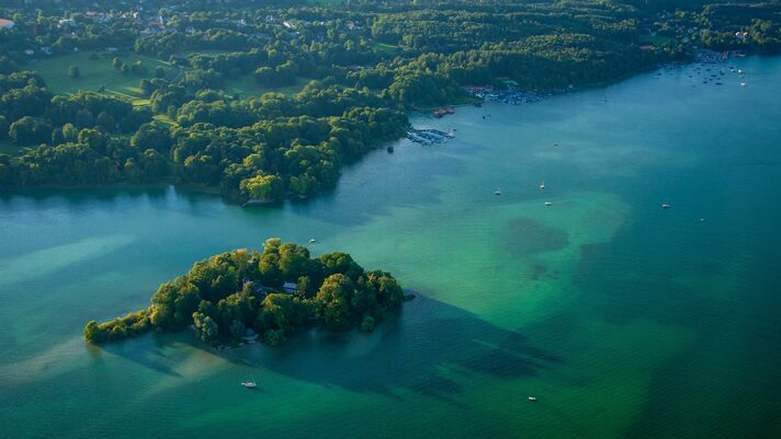 Luftaufnahme einer bewaldeten kleinen Insel, die von türkisgrünem, flachem Wasser umgeben ist.