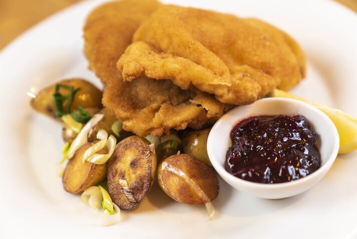 Goldbraun paniertes Schnitzel auf weißem Teller, dazu geröstete Kartoffeln, Gemüse und ein Schälchen Preiselbeeren.