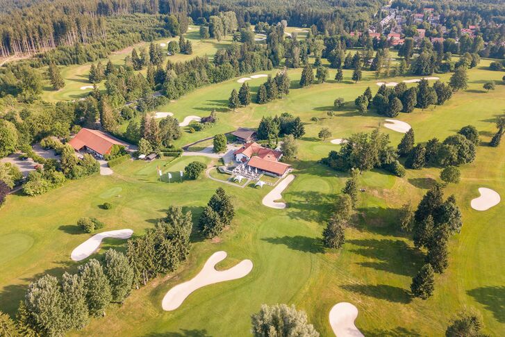 Luftbild einer weitläufigen Golfanlage mit geschwungenen Fairways, hellen Sandbunkern, Baumgruppen und Clubgebäuden mit roten Dächern.