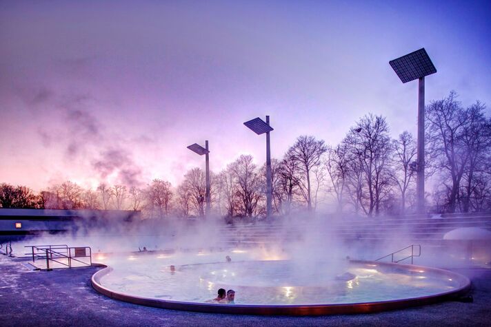 Dampf steigt vom beheizten Freibecken auf, im violetten Dämmerlicht schwimmen einzelne Badegäste.
