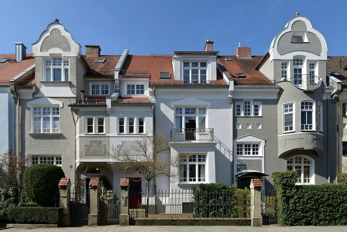 Zwei aneinandergebaute Stadtvillen mit geschwungenen Giebeln und Erkern hinter geschnittenen Hecken.