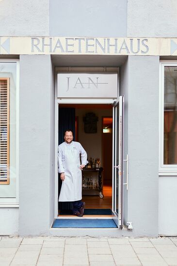 Sternekoch Jan Hartwig in Kochjacke in der geöffneten Eingangstür seines Restaurants JAN.