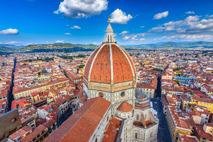 Blick über die Dächer von Florenz auf die rote Kuppel des Doms und den Campanile, dahinter die Hügel der Toskana.