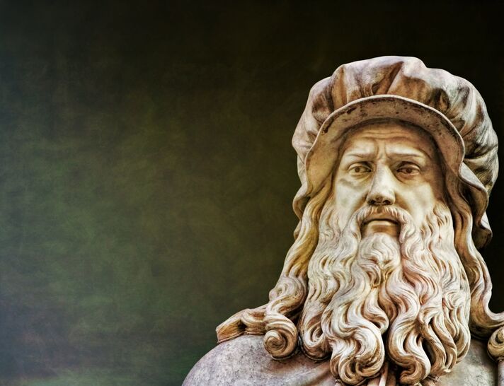 Marmorbüste Leonardo da Vincis mit Kappe und langem Bart vor dunklem Hintergrund.