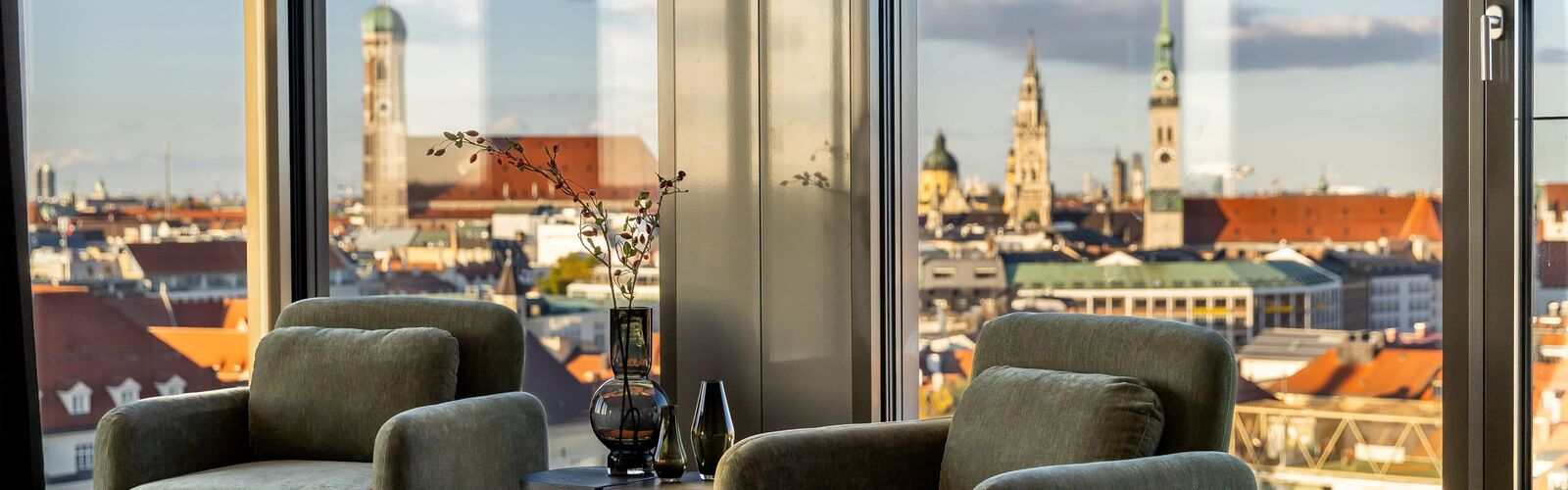 Gemütliche Leseecke mit grünen Samtsesseln und Panoramablick über die Münchner Altstadt