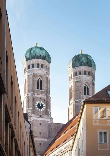 Die beiden Türme der Münchner Frauenkirche mit ihren grünen Kuppeln, gesehen aus einer Gasse der Altstadt.